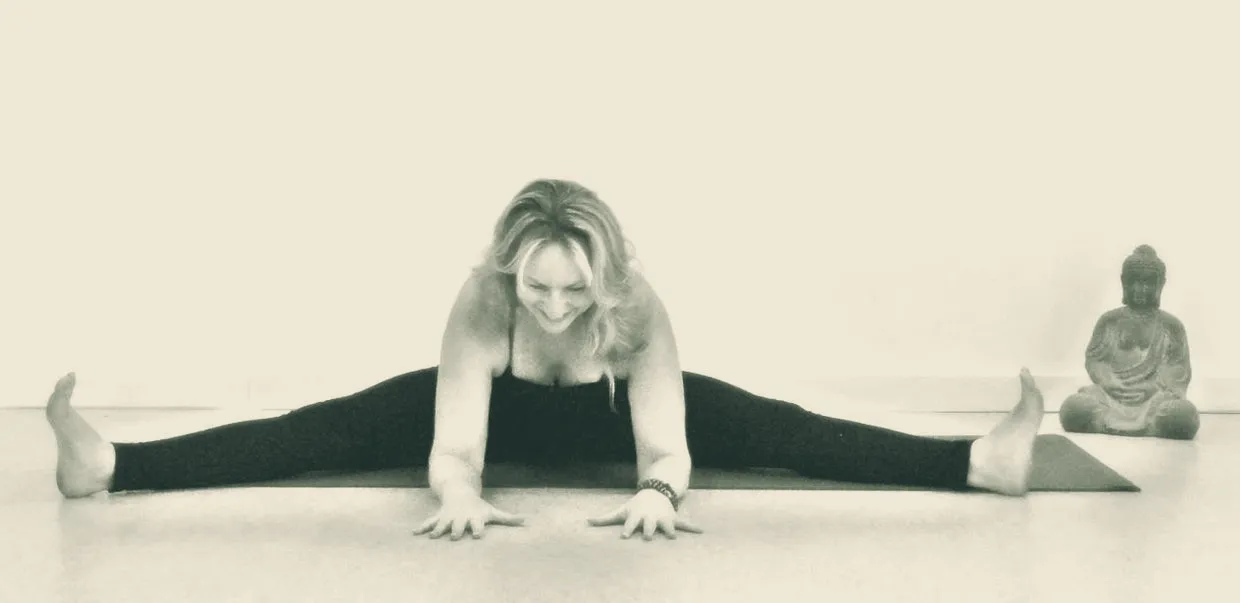 Cheryl Murman in a wide-legged forward fold beside a small Buddha statue at The Chattanooga Yoga Center